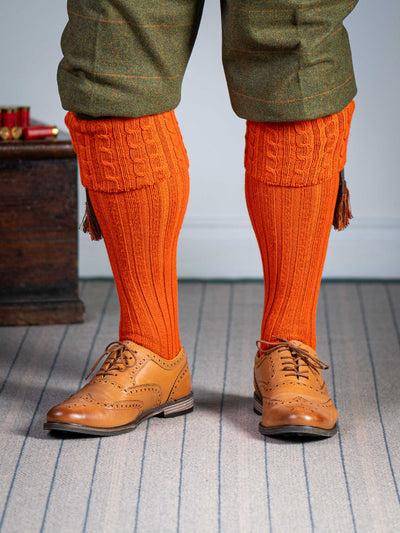 Long knitted shooting socks with a cable turnover in a bright orange nasturtium.