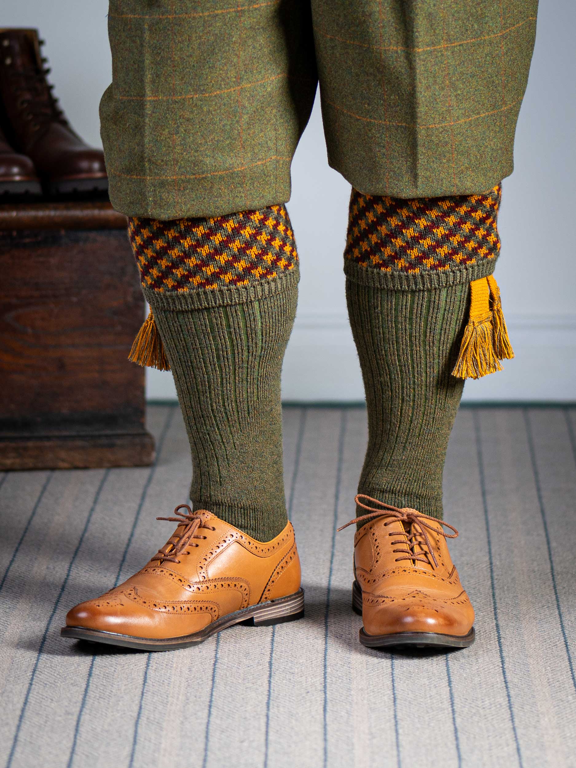A contemporary technical shooting sock with supportive foot arch in dark olive with burgundy and orange pattern in the turnover