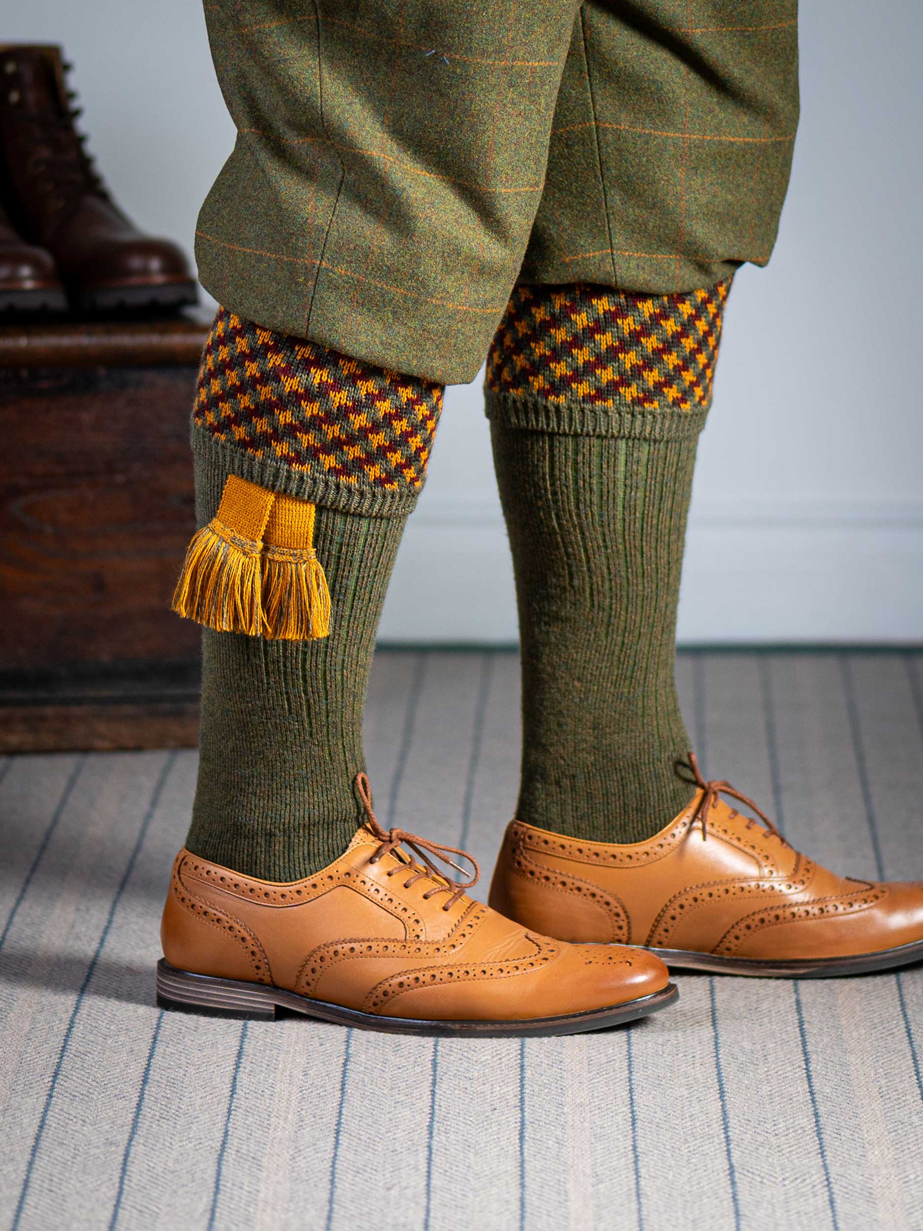 A contemporary technical shooting sock with supportive foot arch in dark olive with burgundy and orange pattern in the turnover