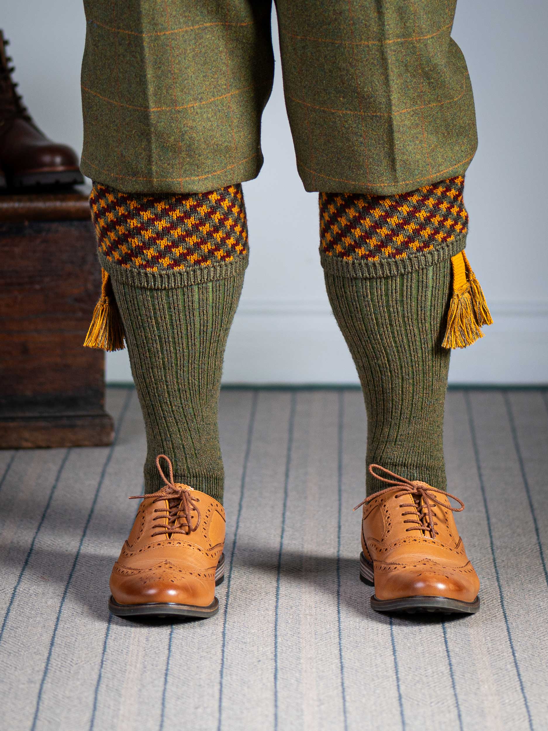 A contemporary technical shooting sock with supportive foot arch in dark olive with burgundy and orange pattern in the turnover